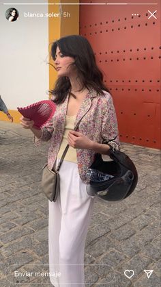 a woman standing on the street holding a fan in her hand and looking off into the distance