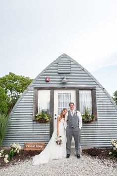 a bride and groom standing in front of a small blue building with flowers on the windows