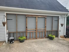 two potted plants sitting in front of a garage door with windows on each side