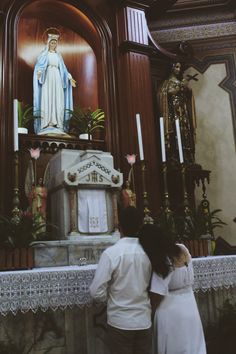 a man and woman standing in front of a church alter with a statue behind them