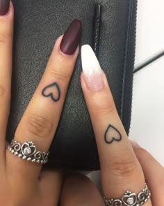 two fingers with hearts tattooed on them, one has a ring and the other has a heart