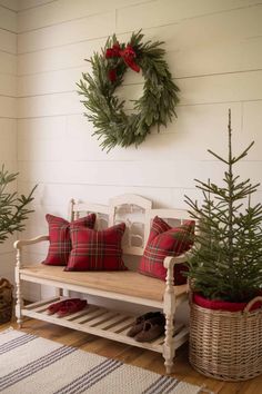 a white bench with red pillows and christmas wreath on the wall above it, next to two small evergreen trees