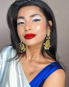 a woman in a blue dress with red lipstick and gold earrings on her face,