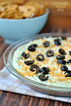 a bowl filled with olives and cheese on top of a table next to a bowl of chips