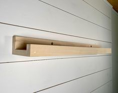 a wooden shelf mounted to the side of a white wall with wood planks on it