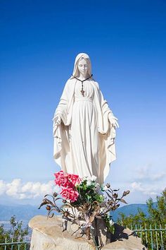 a statue of the virgin mary on top of a rock with flowers in front of it