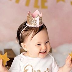 a smiling baby girl wearing a crown and holding two star shaped cookies in front of her face