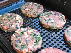 hamburger patties cooking on an outdoor grill with onions and herbs in the center, ready to be grilled