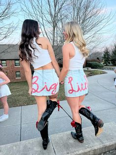 two women in short shorts and cowboy boots holding hands