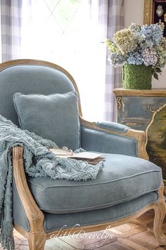 a blue chair sitting in front of a window next to a vase filled with flowers