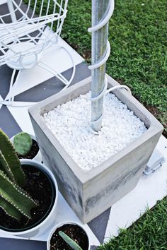 a potted cactus next to two white pots with gravel in them and a metal pole sticking out of the ground