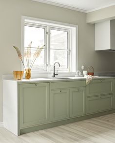 a kitchen with green cabinets and white counter tops next to an open window that looks out onto the outdoors