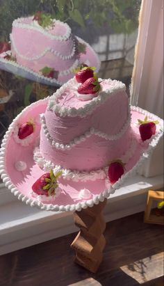 two pink cakes with strawberries on them sitting in front of a window sill