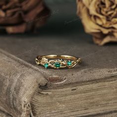 a gold ring with green stones sitting on top of a book