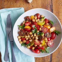 a white bowl filled with tomatoes, chickpeas and spinach on top of a wooden table