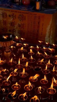 many candles are lit in small bowls on the table