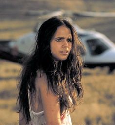 a woman standing next to a white car on top of a dry grass covered field