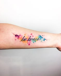 a woman's arm with the words be brave painted on it and watercolor splashs