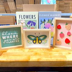 three framed pictures with flowers and a butterfly on them are sitting on a wooden table