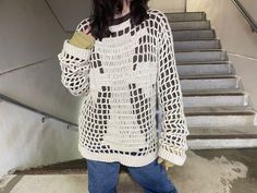 a woman standing in front of some stairs wearing a white sweater and blue jeans with her hand on her hip