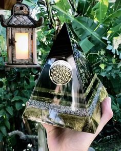 a person holding up a glass pyramid with a flower of life on it and a hanging lantern in the background