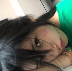 a woman laying on top of a bed next to a green shirt and black hair