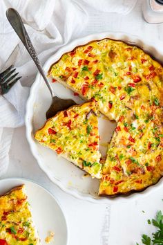 a quiche on a white plate with a slice missing from it and a fork next to it