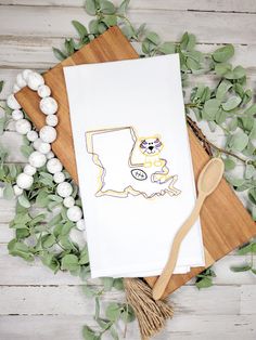 a white towel on top of a wooden cutting board next to green leaves and a spoon