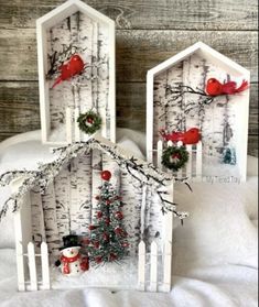 two small houses made out of white birch trees with red birds on the roof and wreaths