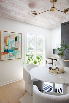 a dining room table with white chairs and a painting on the wall