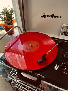 a red record player sitting on top of a metal rack in front of a window