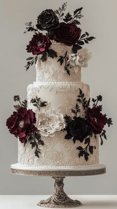 a three tiered wedding cake decorated with black and red flowers on a silver stand