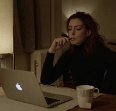 a woman sitting at a table with an apple laptop in front of her and looking at the screen