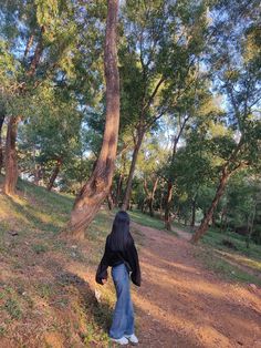 a woman walking down a dirt path in the woods with trees behind her and grass on the ground