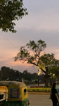 two people walking down the street in front of an old fashioned car and tree at dusk