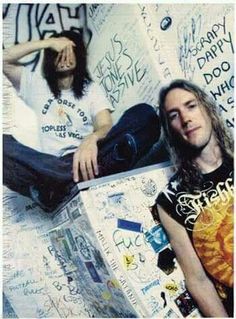 a man sitting on top of a skateboard next to another man with long hair