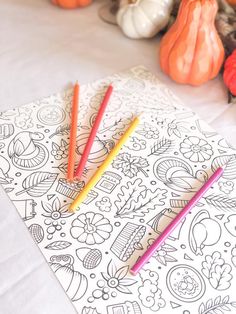 three colored pencils sitting on top of an adult coloring book with pumpkins in the background