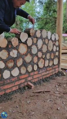 a man that is standing over a wall made out of wood logs and cement blocks