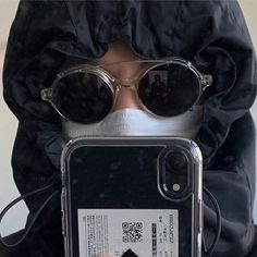 a person wearing sunglasses and holding up a cell phone with a protective cover over their face