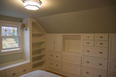 an empty bedroom with white cabinets and drawers in the corner, next to a window