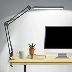 a computer monitor sitting on top of a wooden desk next to a cup and plant