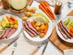 two white plates topped with meat and veggies on top of a wooden cutting board