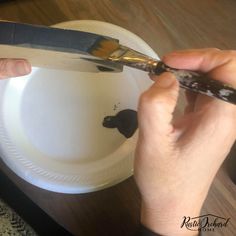 a person is using a pair of scissors to cut paper plates with black paint on them