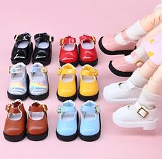 several pairs of baby shoes are displayed on a pink background with doll legs and feet