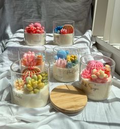 six plastic containers filled with different types of candies on a white sheet covered bed