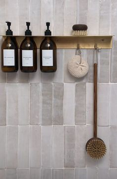 three bottles are hanging on the wall above a brush and soap dispenser