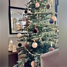 a christmas tree with ornaments hanging from it's branches in front of a window