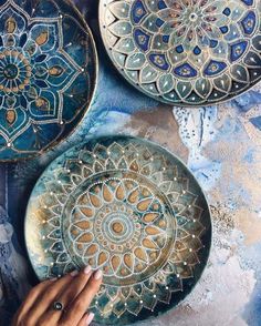 three plates with designs painted on them are being held by a person's hand