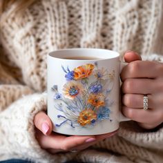 a woman holding a coffee mug with flowers painted on the outside and inside, in her hands