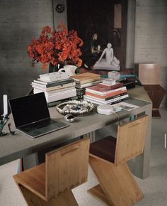 a laptop computer sitting on top of a wooden table next to books and flowers in a vase